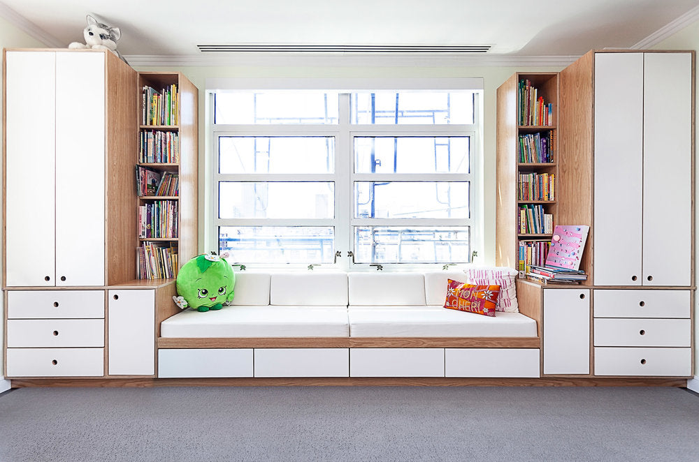 Cozy window seat with cushions, surrounded by bookshelves and cabinets