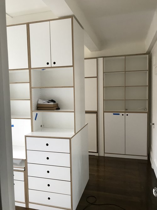 Modern white cabinetry in a room, featuring a tall unit with shelves and drawers for storage.