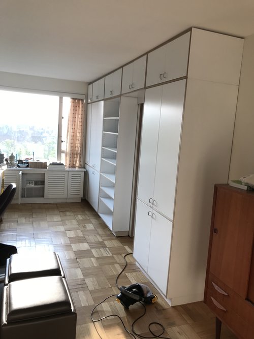 Room with large white wardrobe cabinets along one wall, a vacuum cleaner on the tiled floor.