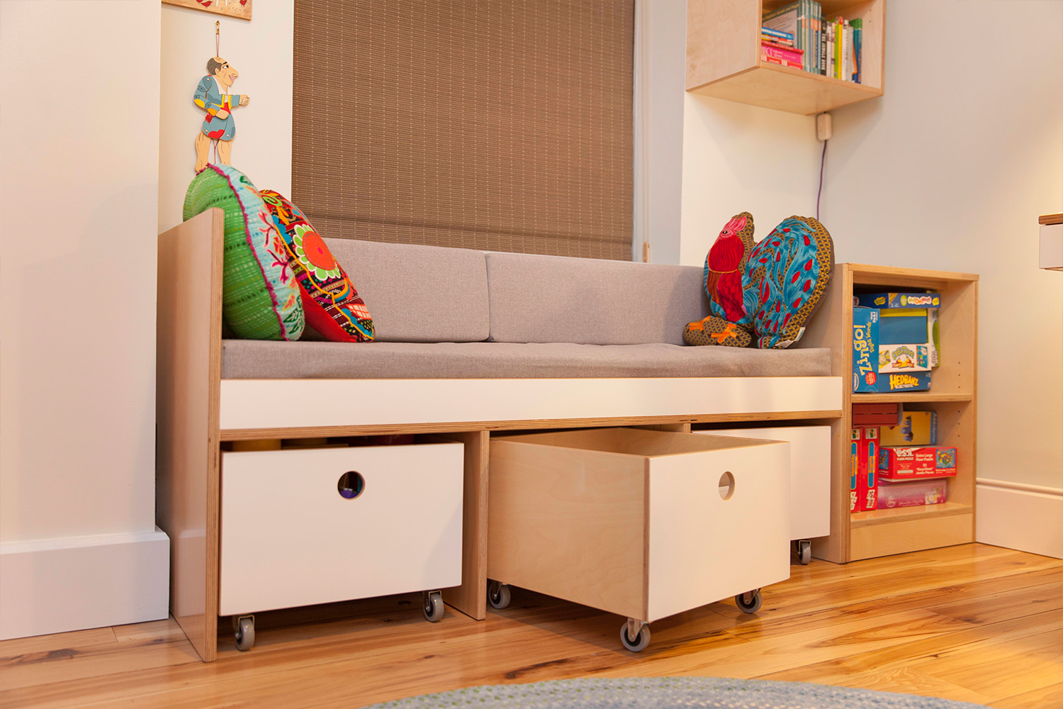 Gray sofa nook, colorful cushions, storage drawers, children’s books.