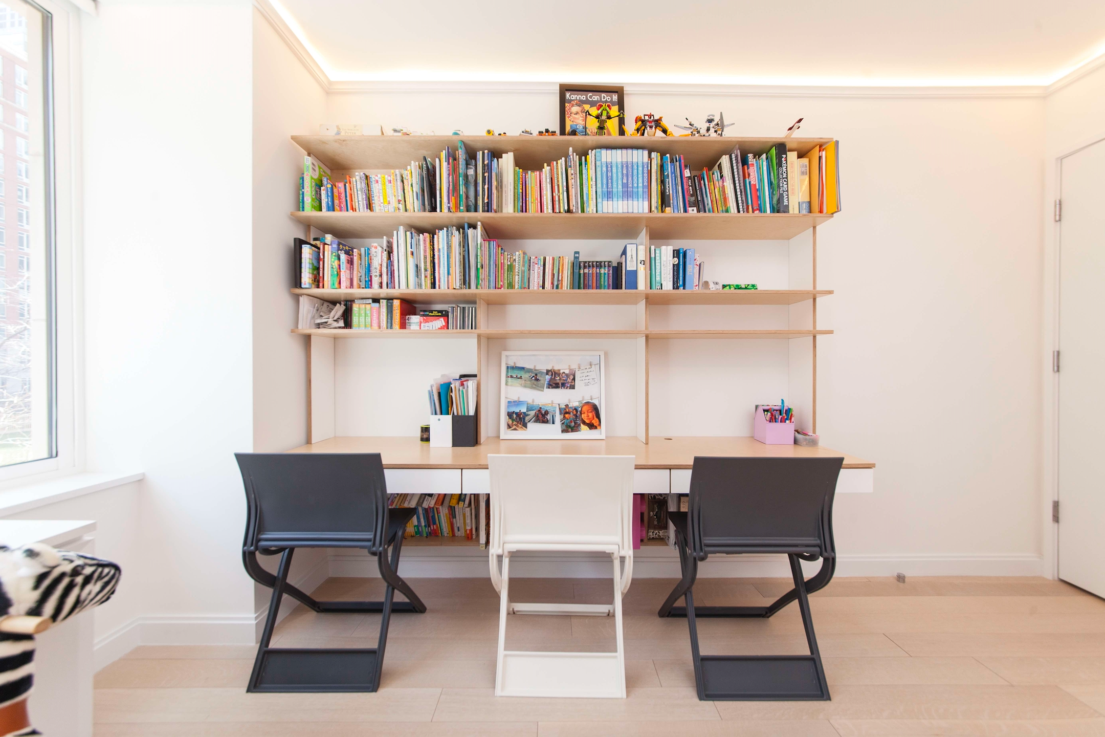 Modern study area with a white desk, two chairs, and a large bookshelf filled with colorful books.