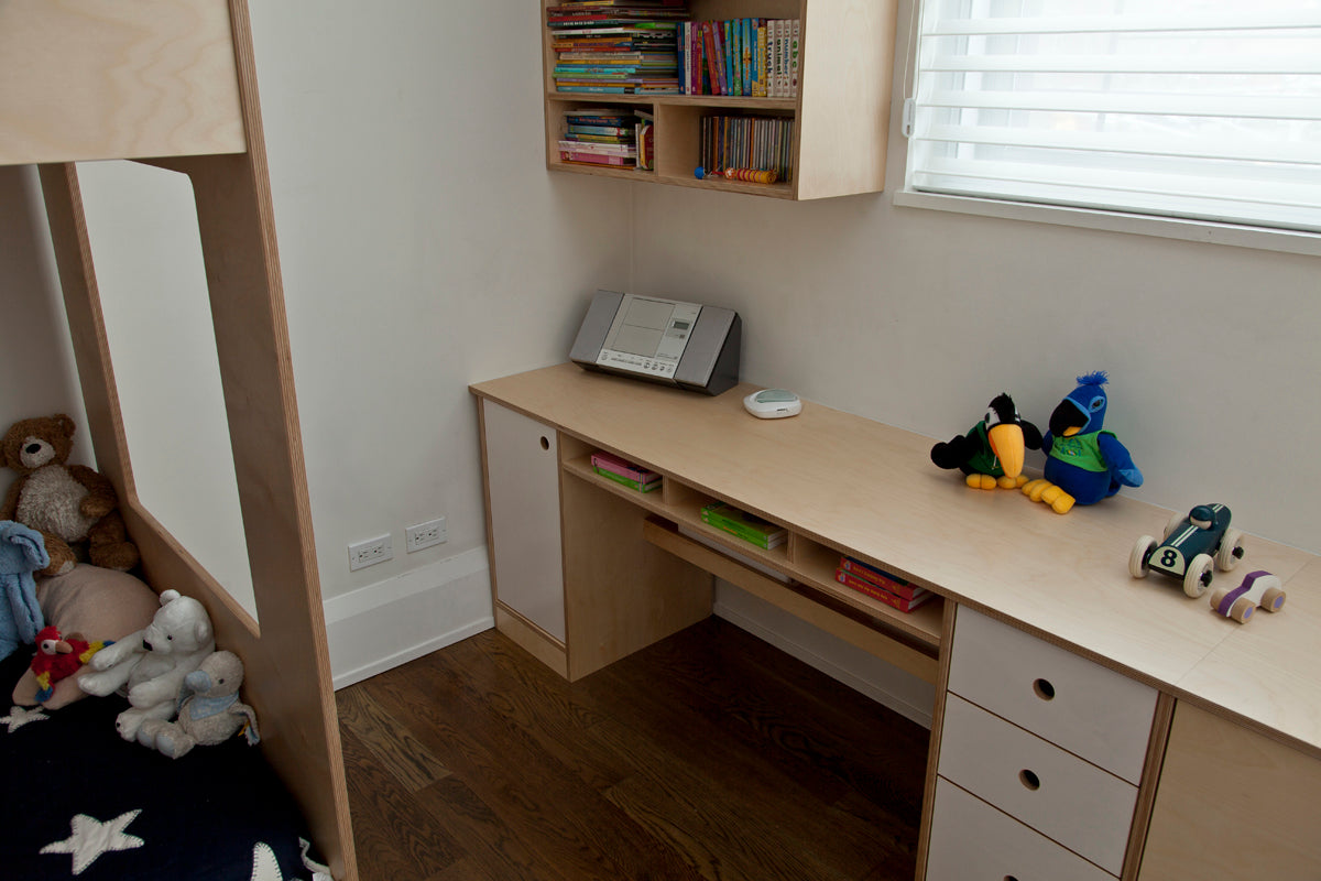 Child's study area with desk, toys, and bookshelves under a window in a neatly organized room.