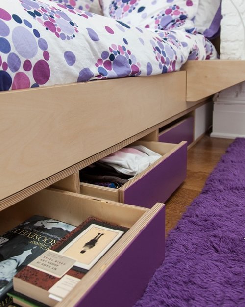 Close-up of open storage drawers under a bed with a colorful floral comforter and purple rug.