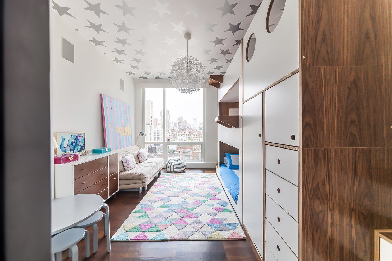 Child’s room with starry ceiling, city view, colorful rug, wooden furniture.