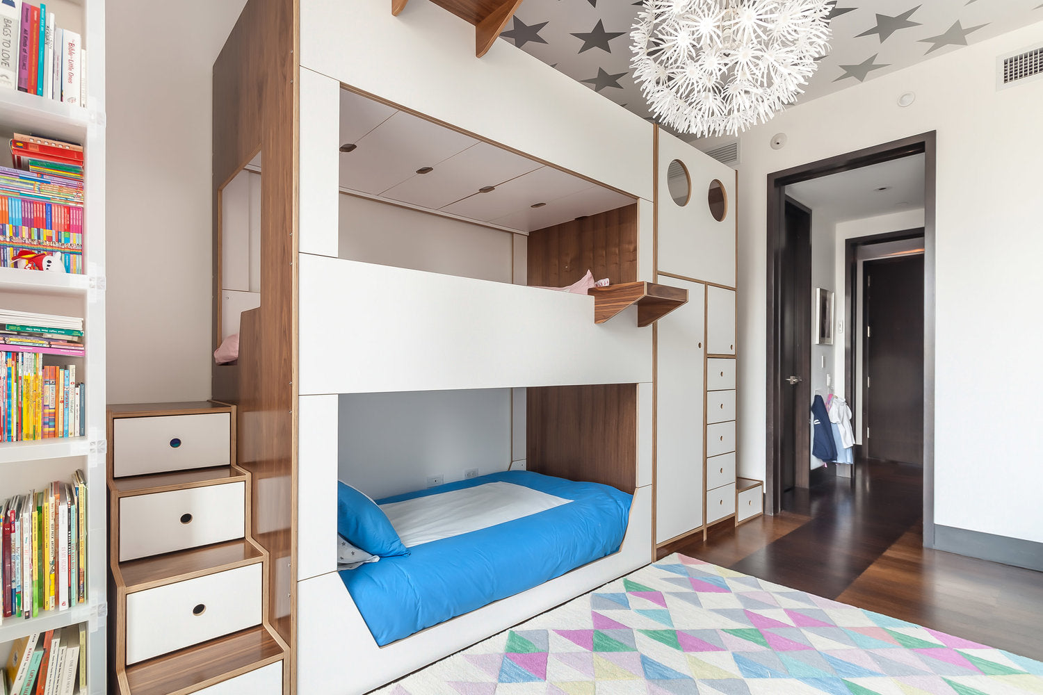 Triple bunk bed with star ceiling and colorful rug in a bright room.