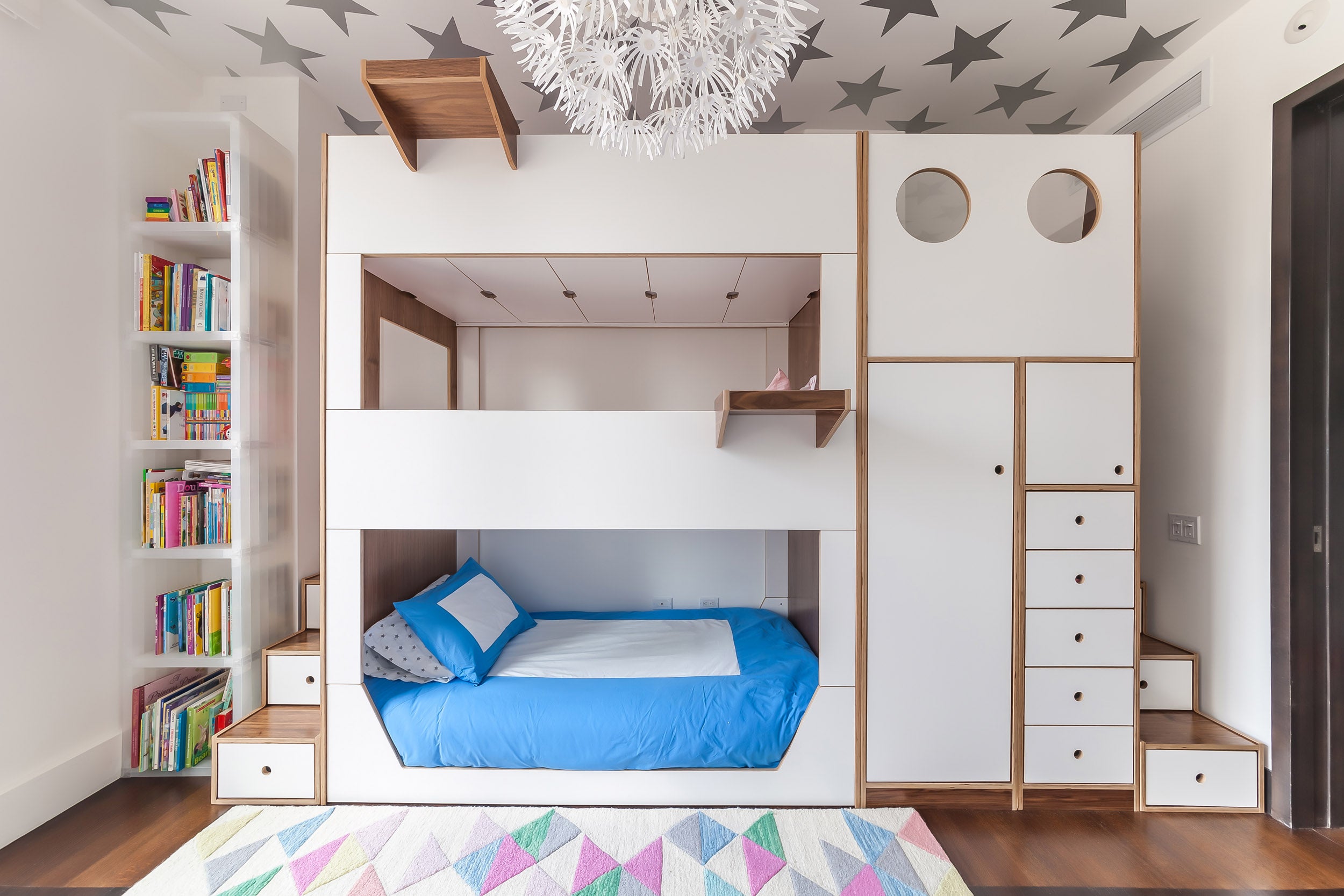 Modern kids' room with a white bunk bed, built-in storage, star-patterned ceiling, and colorful rug.