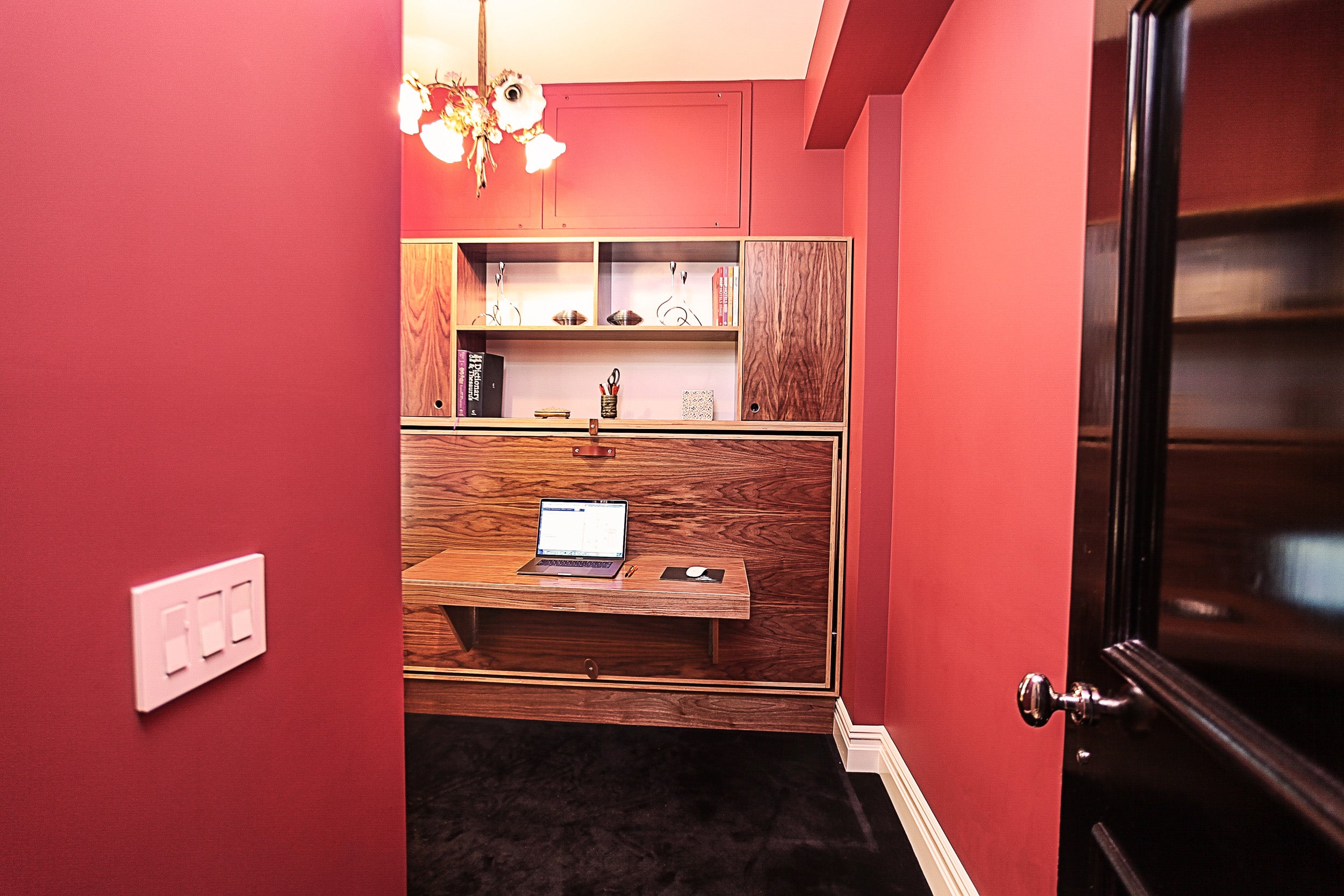 Red wall, wooden cabinet, laptop on shelf.