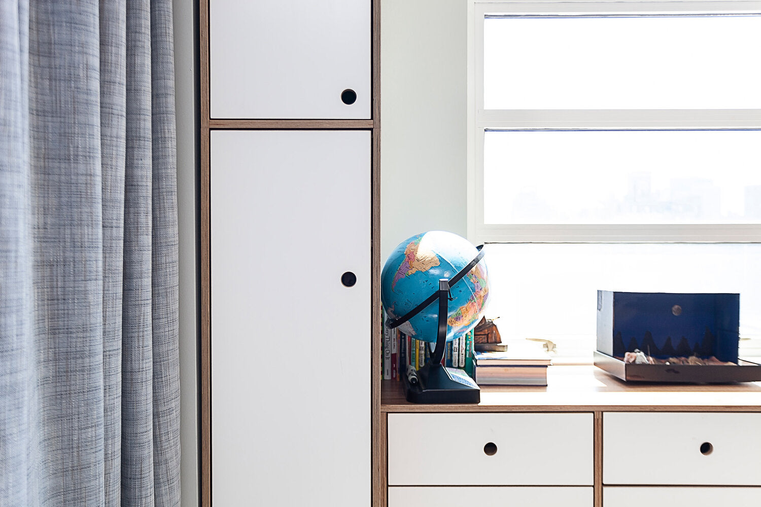  A globe and books on a shelf by a window with curtains.