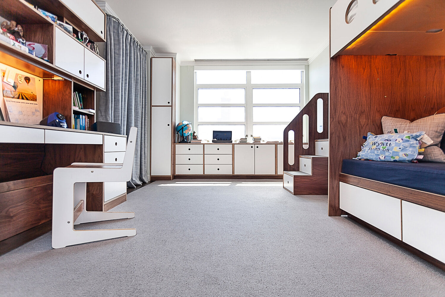 Modern child’s room with white, wooden furniture, toys on shelves, and a bright window.