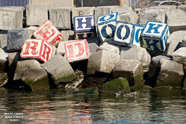 Colorful blocks spell ‘HERO’ on a rocky shore, symbolizing strength and tribute.