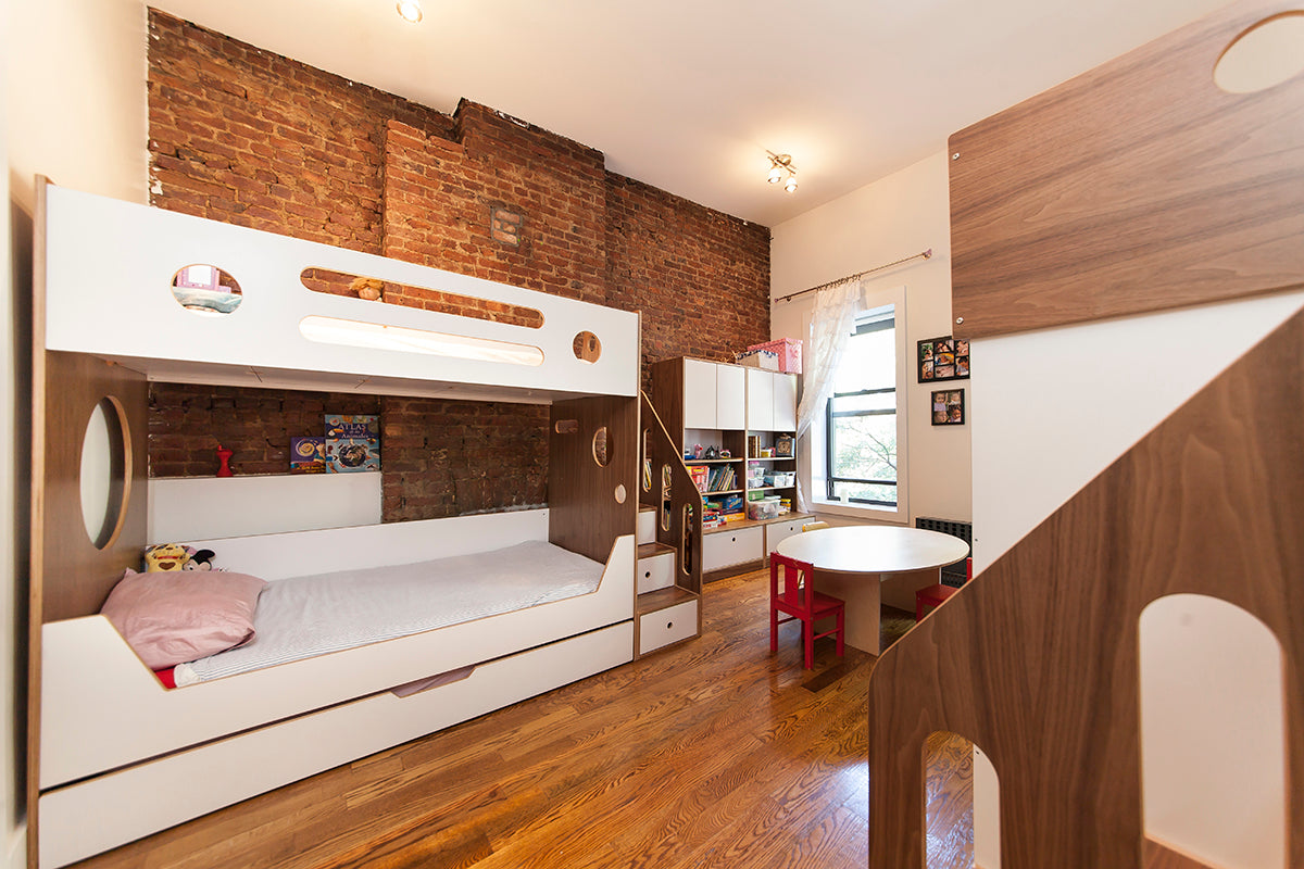 White bunk bed with circular windows, brick wall, and wooden floor in a cozy room.