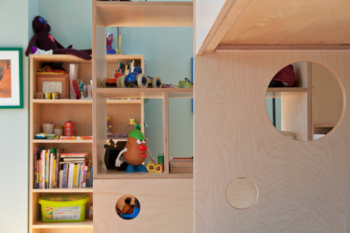 Cozy play area with wooden house, shelves of books and toys, and a seated person in the background.