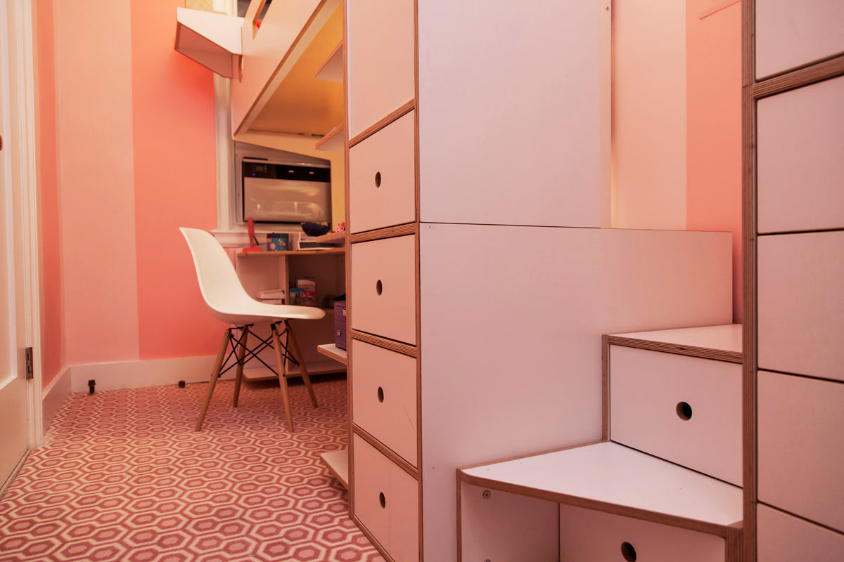 Pink room with desk under loft bed, open drawers, and white chair.