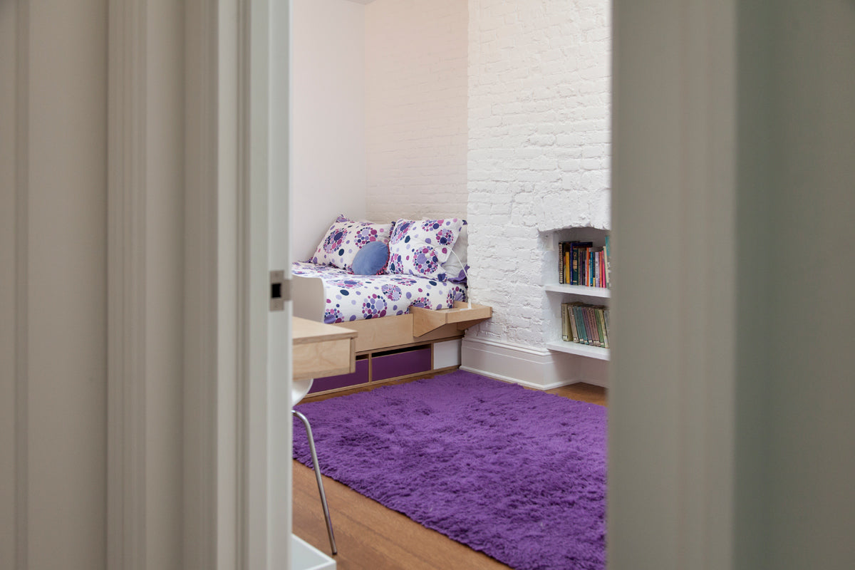 Cozy room, purple rug, white brick wall, floral sofa pillows.