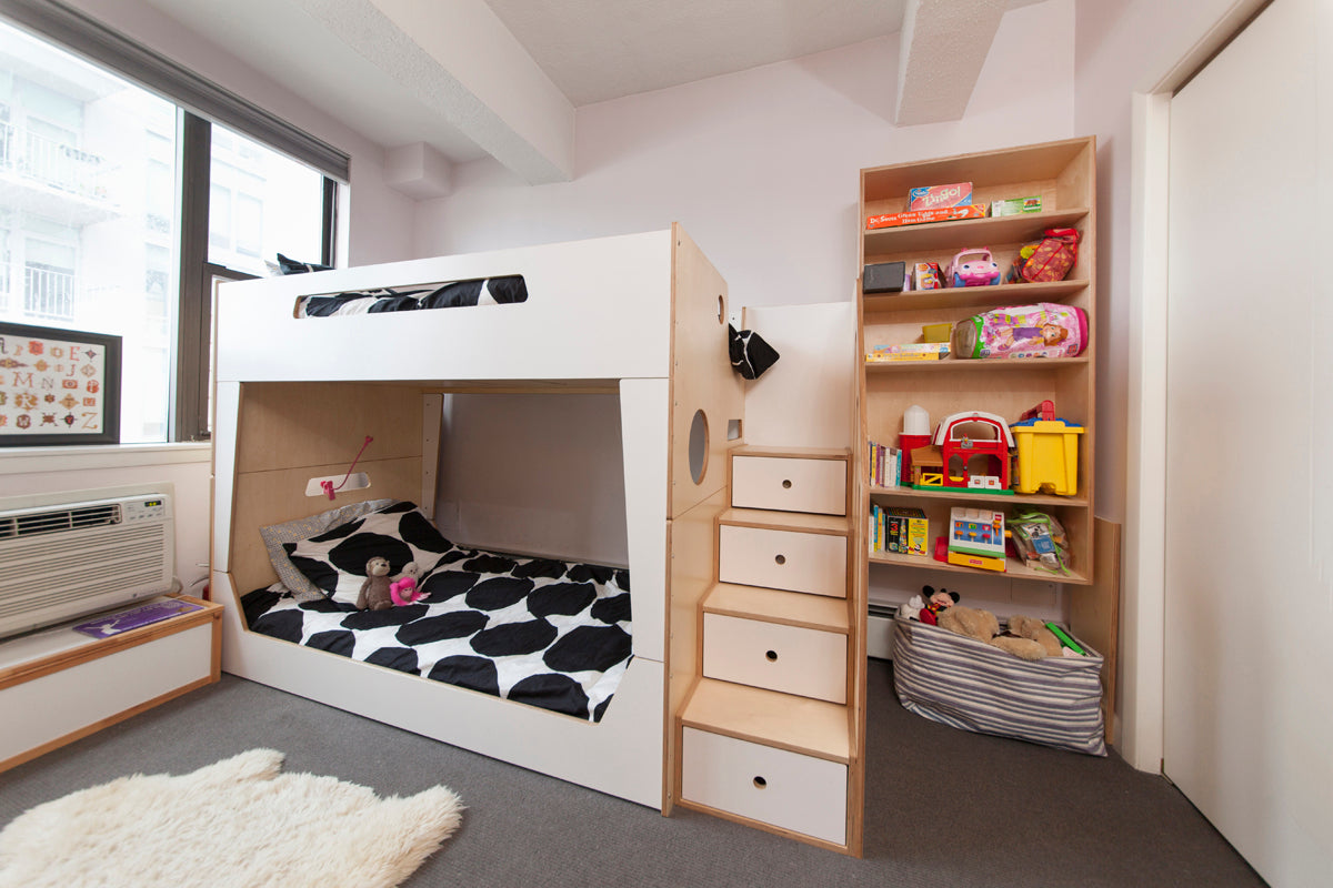 Child’s room with loft bed, storage stairs, toys, shelves, white rug.