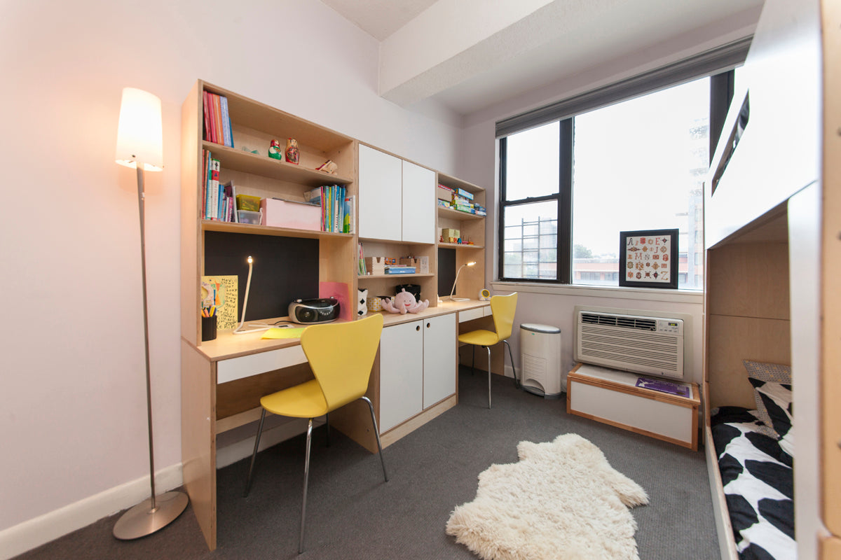 Cozy study room with desk, chairs, lamp, window, and bookshelf for two children.