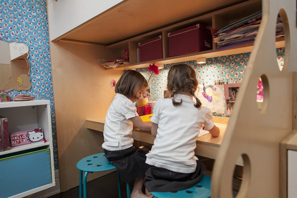 Two children studying at a built-in desk in a colorful bedroom with a floral wallpaper background.