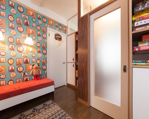 Vibrant child's room with a red bed, decorative wall filled with colorful prints, and sliding doors.