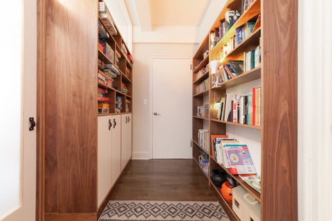 Narrow hallway lined with wooden bookshelves filled with a variety of books, leading to a white door.
