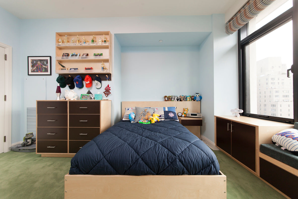 Tidy bedroom, large bed, dresser, shelves with toys, city view from window.