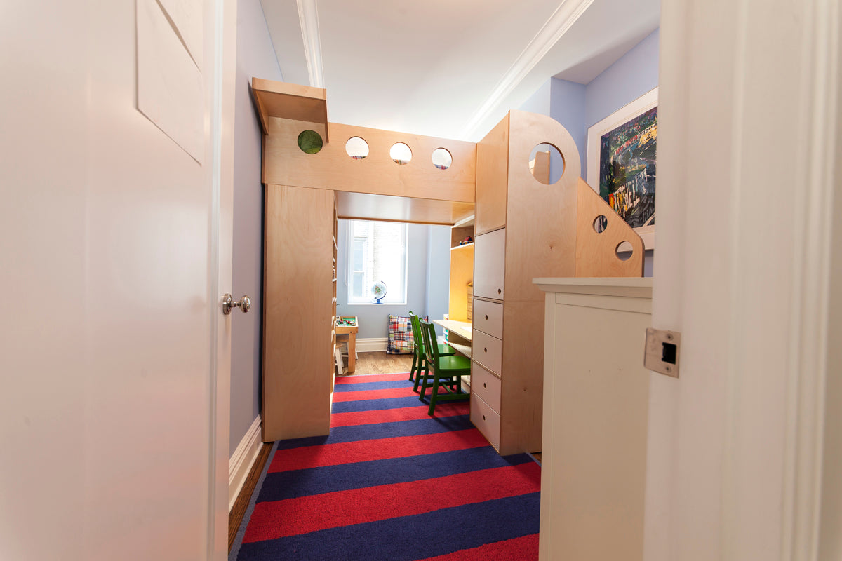 Hallway with wooden cabinets, colorful rug, leading to a bright room.