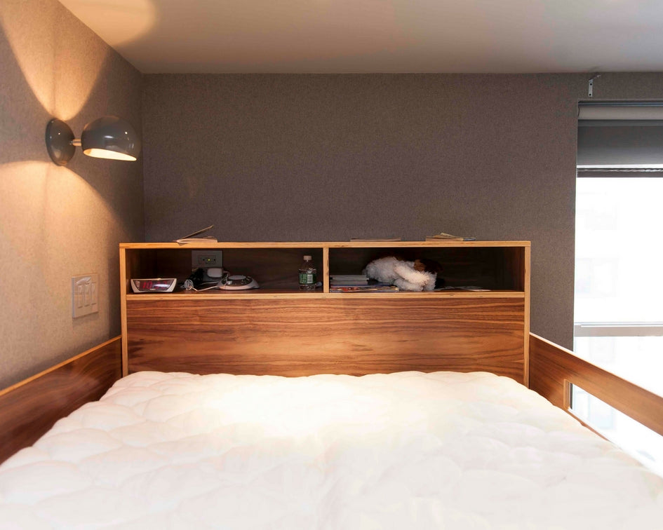 Cozy bedroom, white bedding, wooden headboard shelf, resting cat.