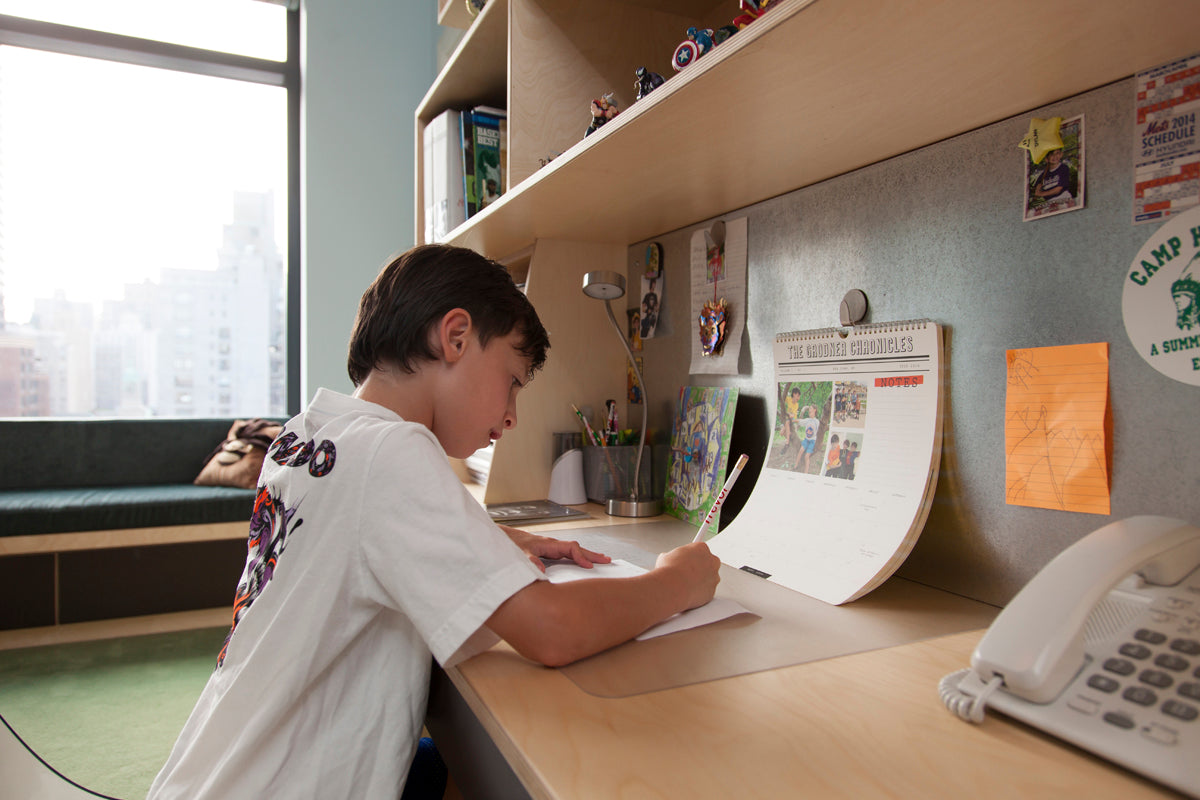 Child at desk with books, papers, studying, phone present, educational setting.