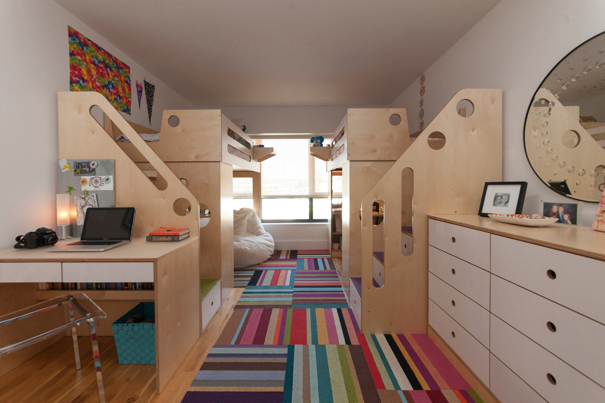Modern kids’ room with bunk beds, desk, colorful rug, and white drawers.