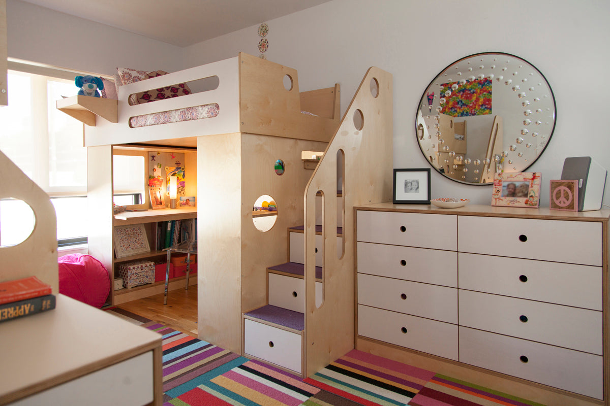 Cozy room with custom wooden loft bed, built-in desk and drawers, colorful rug on the floor.