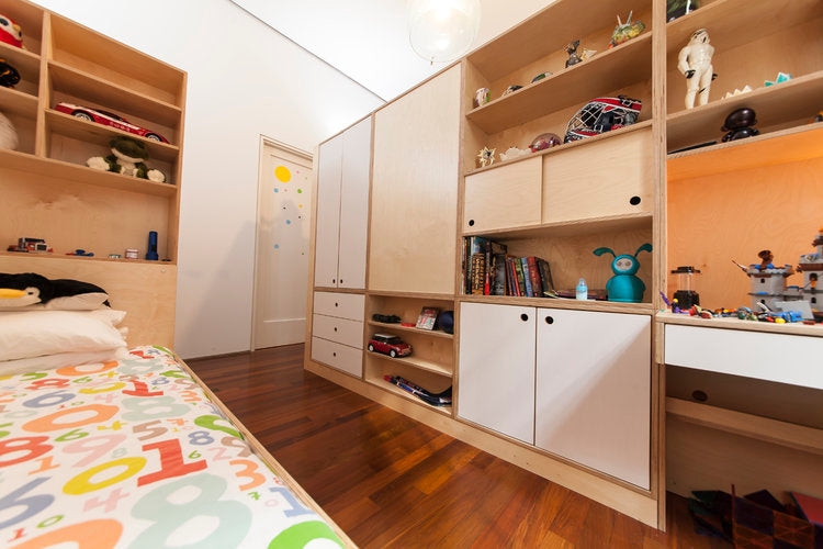 A child's room with a colorful bedspread, wooden storage units filled with toys and books, and warm lighting.