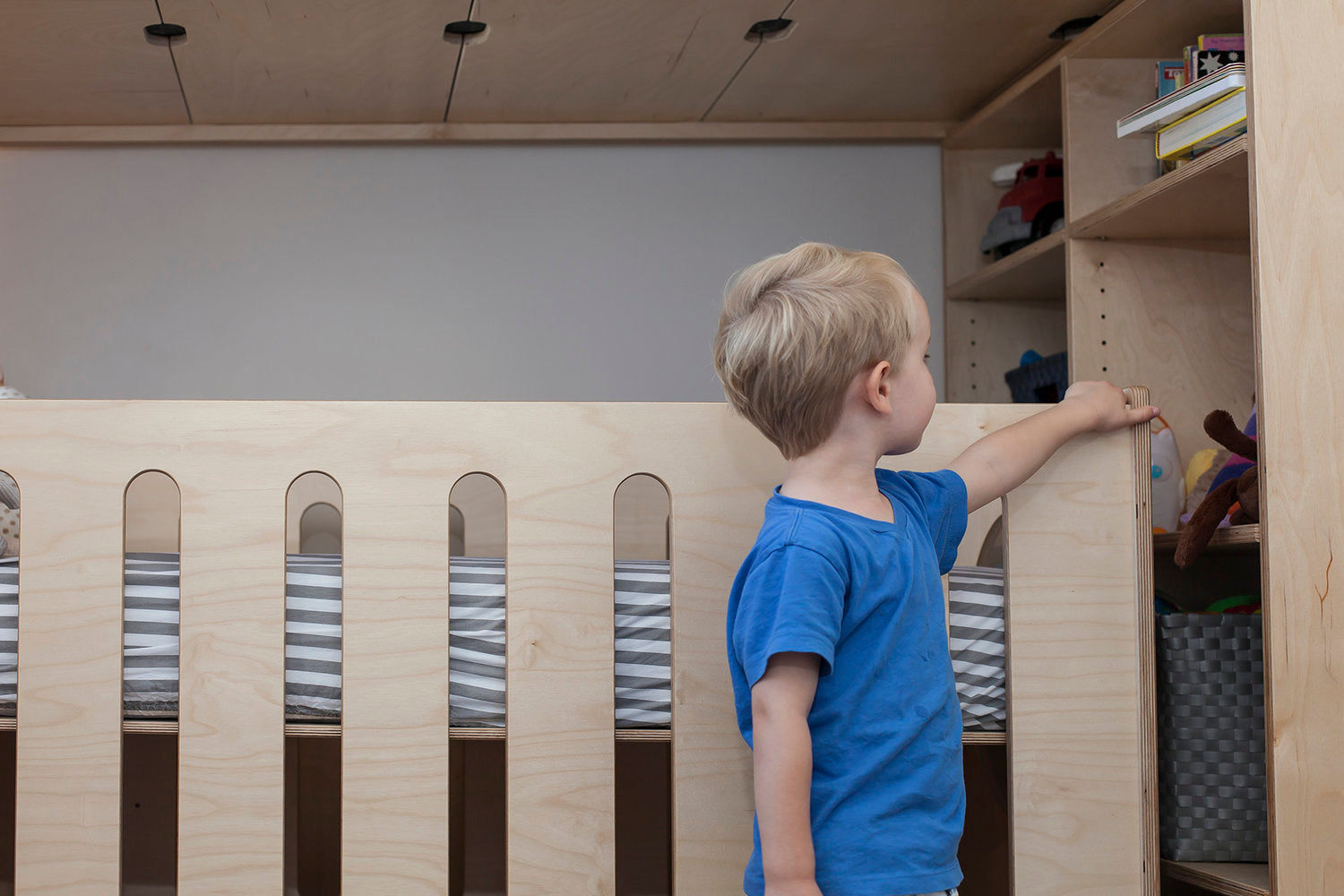 Child in blue shirt reaching for shelf on wooden bunk bed with books.