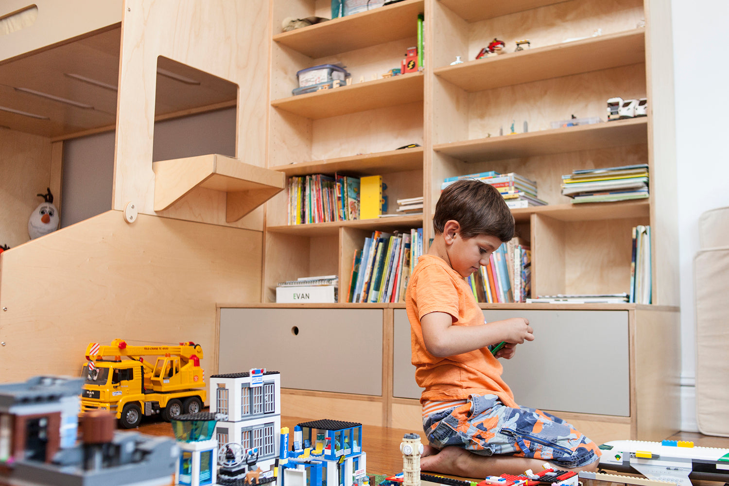 Child in tidy room plays with toys, bookshelves in background.