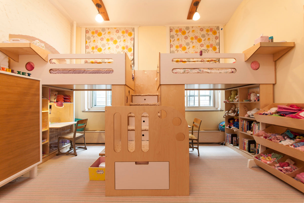 Brightly lit children's room with custom wooden bunk beds, shelves full of toys, and a study area.