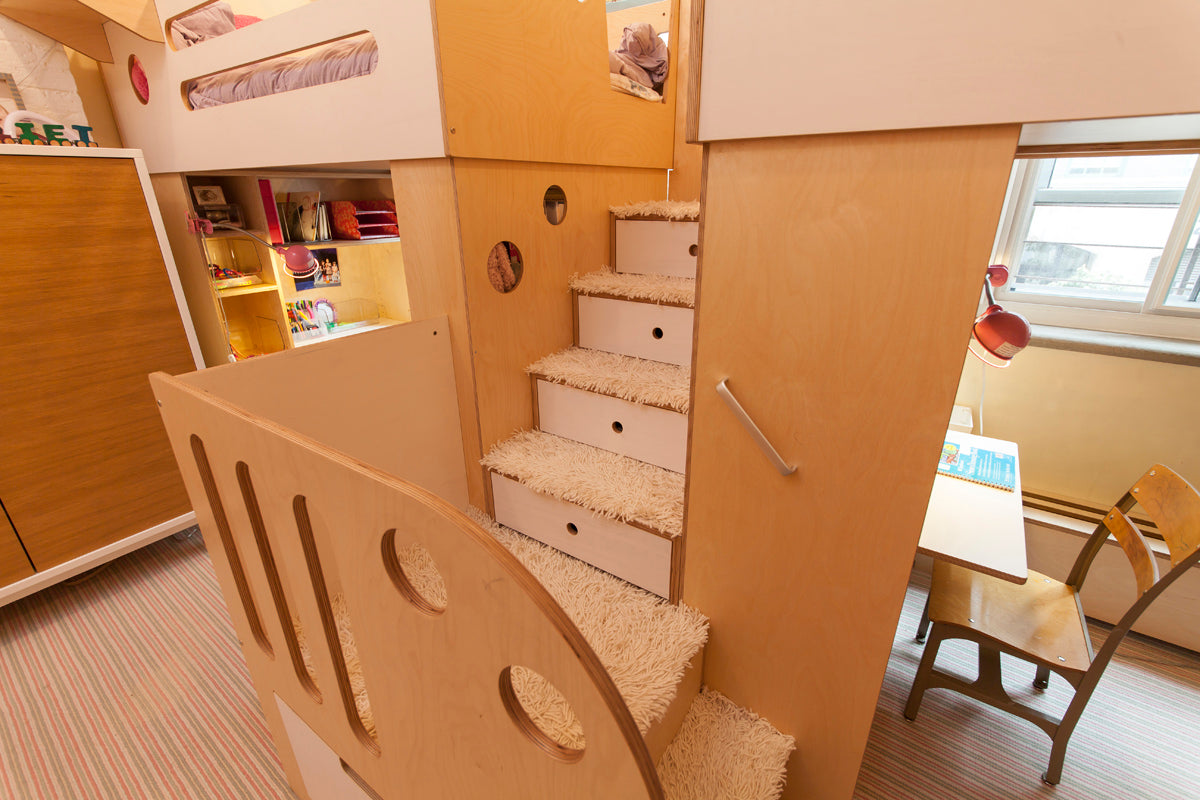 Elevated view of a child's room featuring wooden steps leading to bunk beds and a study area by the window.