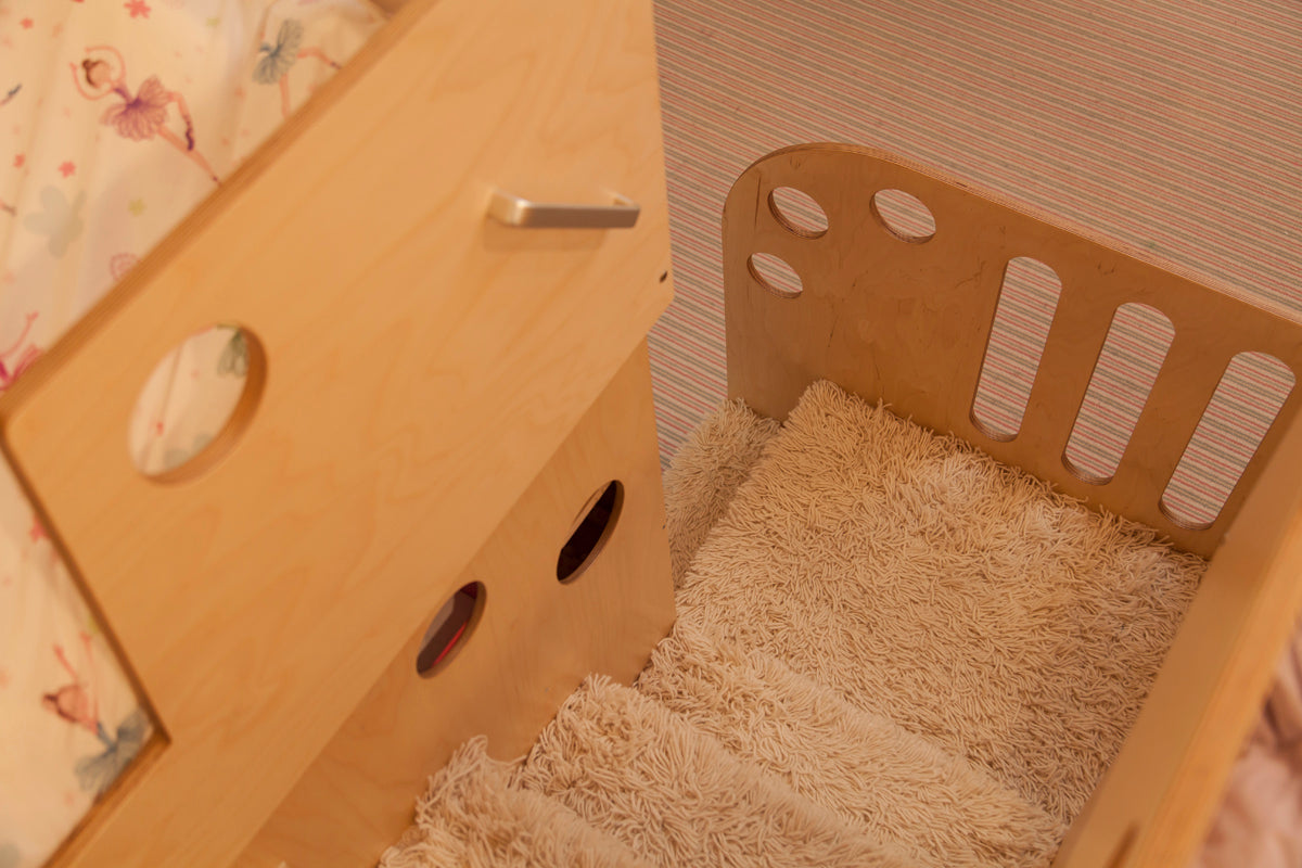 Close-up of a cozy children's bed nook with shaggy bedding and a wooden guardrail with round cutouts.