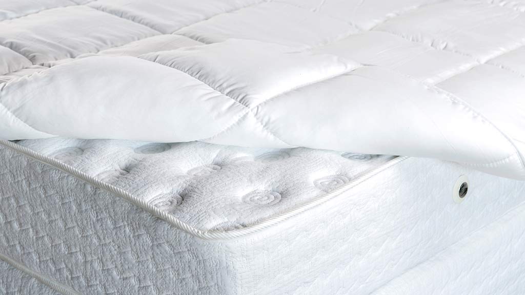 Close-up of a white mattress with a plush mattress topper and detailed stitching on the surface.