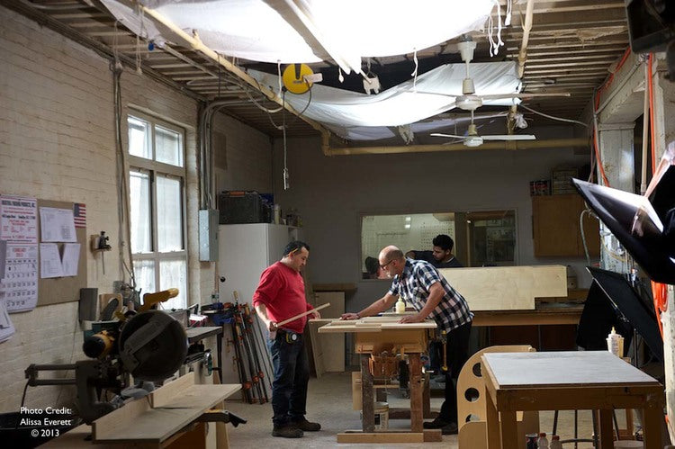 People working in a woodshop with various tools and lumber