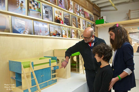 Man showing furniture to two kids in a workshop with designs and photos on the background wall.