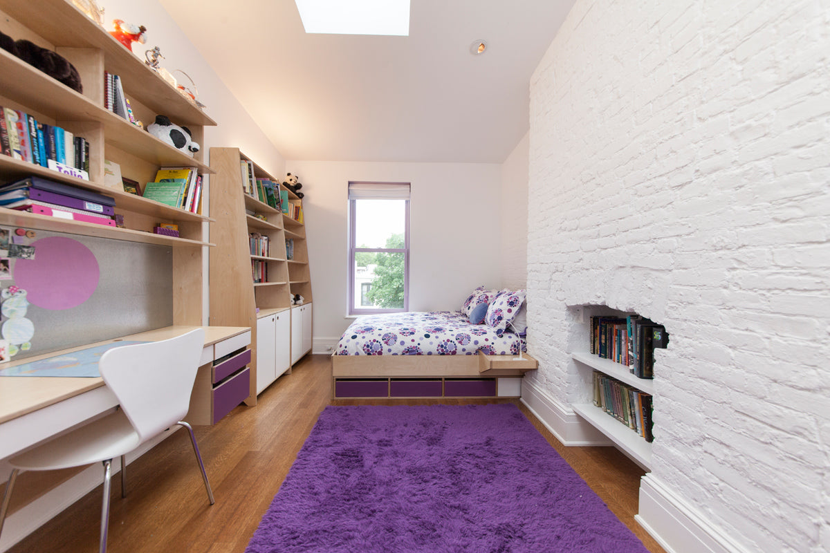 Cozy bedroom with bed, desk, bookshelves, purple rug.