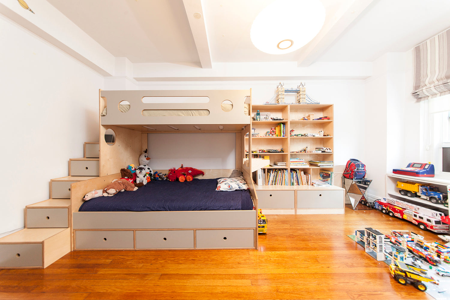 A cozy child’s bedroom with a bunk bed, bookshelf, toys, and a wooden floor.