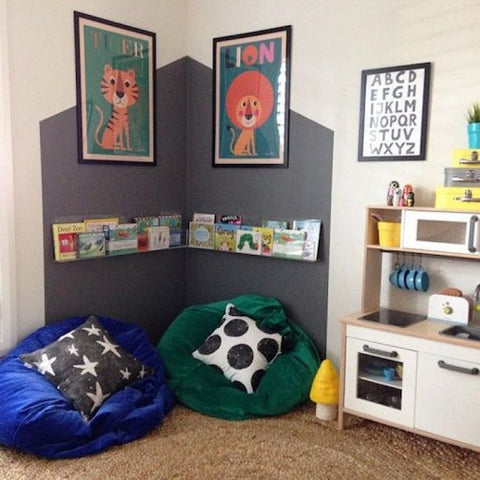 A cozy reading nook with colorful bean bags, a bookshelf, and vibrant animal posters on a gray wall.