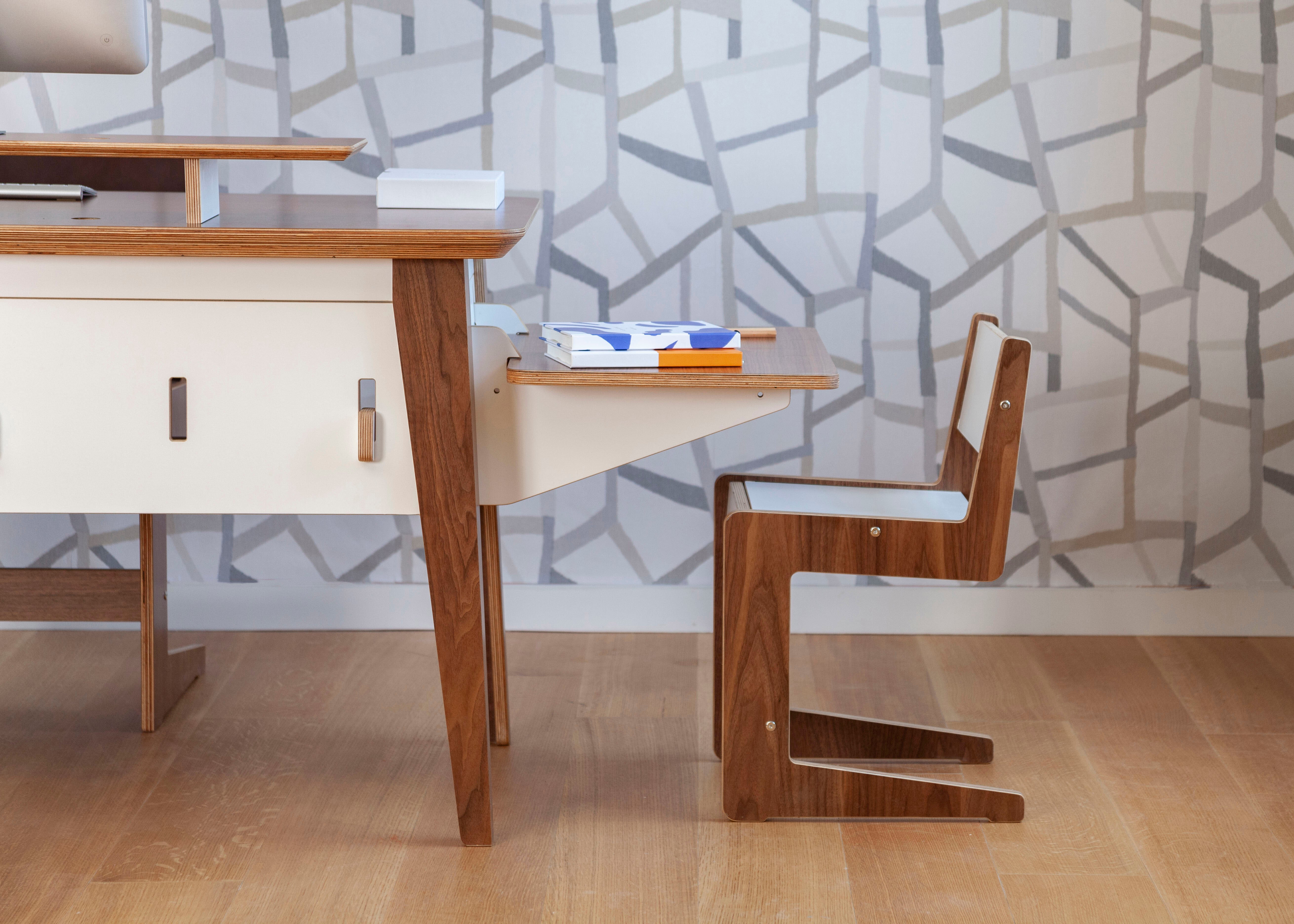 Modern wooden desk and chair on a hardwood floor against a geometric patterned wallpaper backdrop.