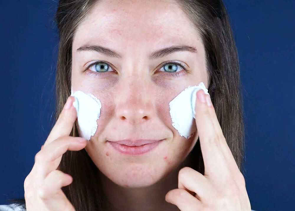A woman using Clear Out with zinc oxide for acne by SLMD Skincare