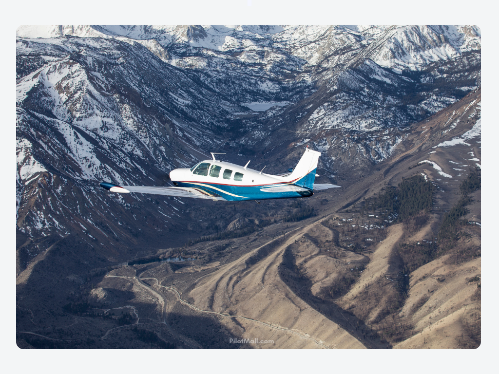 A White and Teal Beechcraft Bonanza Flying Over Snowy Mountains - Pilot Mall