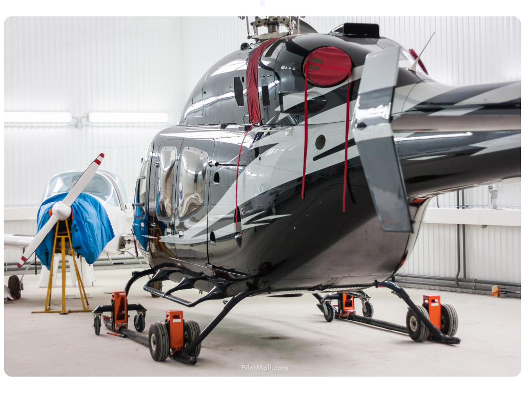 A helicopter and a single engine plane stored in a hangar with a rotary wing aircraft cover- Pilot Mall