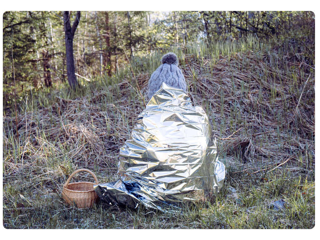 A woman out in the woods wrapped in an emergency blanket - Pilot Mall