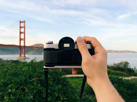 A hand holding a camera points from Presidio Park in San Francisco at the Golden Gate Bridge
