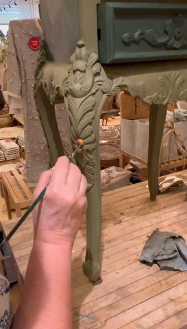 A person from The Owl Box painting the leg of a side table with chalk paint.