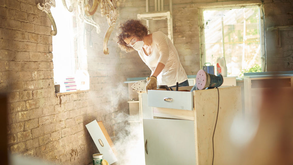 A person with safety equipment busy sanding a cabinet.