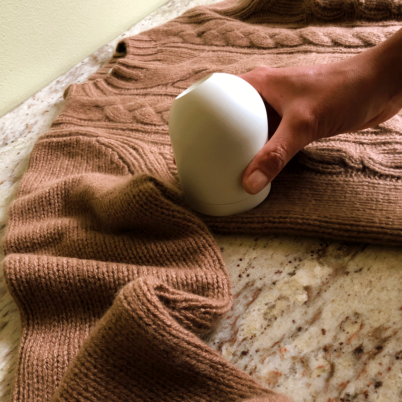 A gif of a hand running a dome shaped fabric shaver across a cashmere sweater